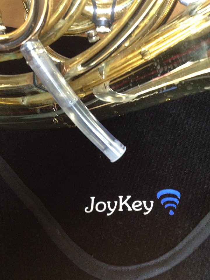 a ten centimeter long drop catcher tube half full of water drained from a JoyKey automatic water drainage spit valve on the lead pipe in front of a black lapcloth with the JoyKey logo on it